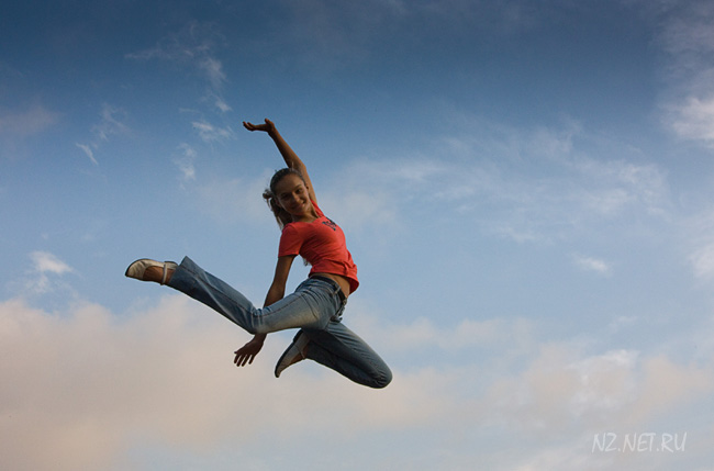 Девушка в прыжке на фоне синего неба с облаками