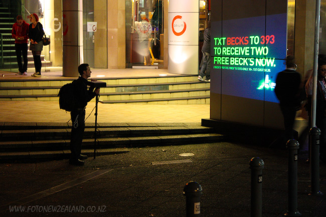 Парень проецирует рекламу пива на улице с помощью переносного проектора